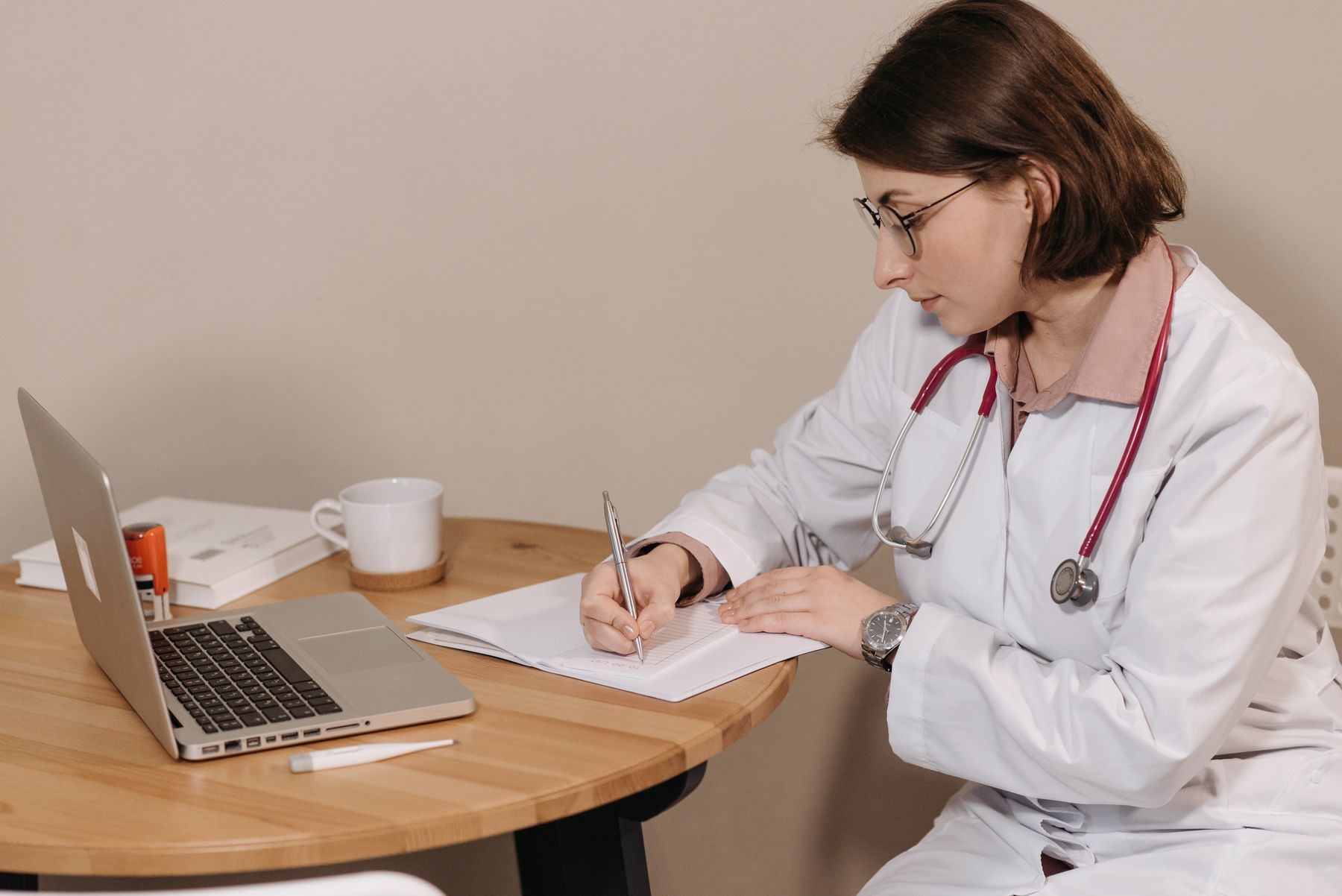 Clinician writing notes beside a laptop in a quiet office